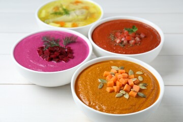 Tasty broth and different cream soups in bowls on white wooden table, closeup