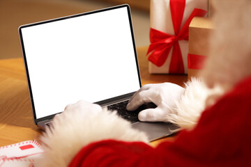 Santa Claus using laptop near Christmas gifts at table, closeup