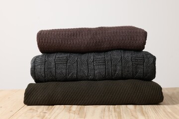 Stack of casual sweaters on wooden table against light background