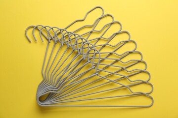 Empty hangers on yellow background, top view