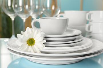 Set of clean dishware and flower on light blue table, closeup