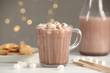 Cup of aromatic hot chocolate with marshmallows and cocoa powder on white table, closeup