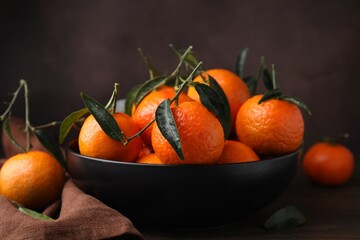 Fresh ripe tangerines with green leaves in bowl on table, closeup