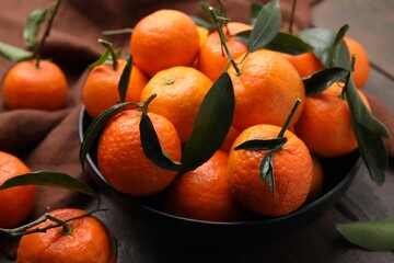 Fresh ripe tangerines with green leaves in bowl on table, closeup