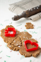 View of gingerbread cookie dough with Christmas molds on table with floured rolling pin on cloth, soft background, vertical, with copy space