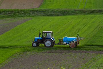 Fototapeta premium Aerial view of tractor spraying crop in green farm fields with pesticide