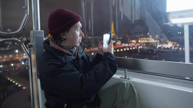 Tourist in a red hat takes pictures of the Eiffel Tower on a mobile phone at night, Paris, France