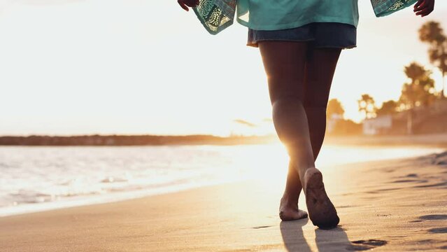 Close up and portrait of legs of one young Afroamerican woman walking and running having fun enjoying on the sand of the beach with the sunset at the background
