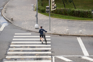 Man crosses the road at a pedestrian crossing and carries a bicycle next to him. View from above.