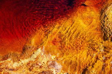 Detail of the rocky bottom and water ripples of the Rio Tinto (Spain). The red colour of the river is due to the dissolution of minerals (oxides and iron) that occurs because its water is very acidic - obrazy, fototapety, plakaty