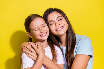 Photo of cheerful dreamy small siblings dressed t-shirts closed eyes hugging smiling isolated yellow color background