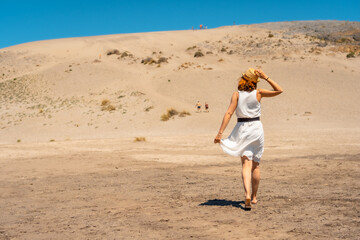 Woman walking along sand dune against blue sky
