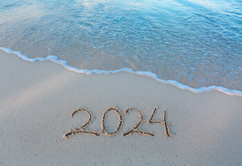 New Year 2024 handwritten in the white sand surface.