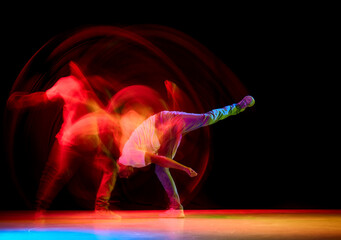 Young sportive guy dancing hip-hop, breakdance against black studio studio background in red neon...