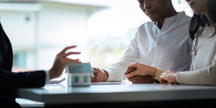 Young Asian couple making contract with house sale agency. man and his wife sitting signing the contract next to him looking the contract document with smile. real estate agreement successful concept