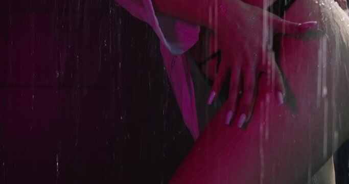 Close-up of wet woman moving her hand slowly across the body. Erotic woman in lingerie and shirt stands in the shower, water drops flow down the body. Provocative woman sensual moves. Slow motion
