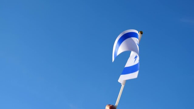 Hand waving Israel Israeli flag against clear blue sky, close-up view, slow motion.