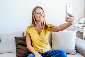 Happy young women using a mobile phone sitting on a couch in the living room at home.