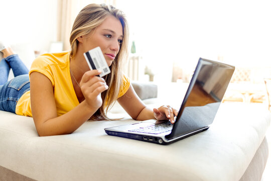 Shot of a cheerful young woman doing online shopping while seating on a couch at home during the day. Cropped shot of a young woman using a credit card to make an online payment at home.