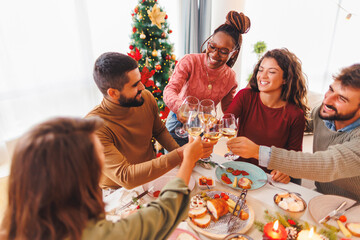 Friends making a toast raising glasses of wine while having Christmas dinner at home