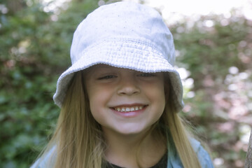 Candid headshot of adorable little girl wearing bucket hat in the forest, spending time in the nature, outdoors experience in the countryside	