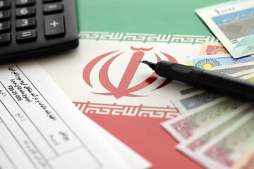 Iranian annual income tax return form F20-25-006 ready to fill on table with pen, calculator and iranian money on flag close up - obrazy, fototapety, plakaty