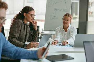 Group of young business people discussing something while sitting at the office table