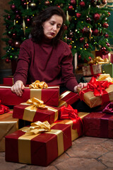 Tired young woman in front of the Christmas tree and boxes with gifts....
