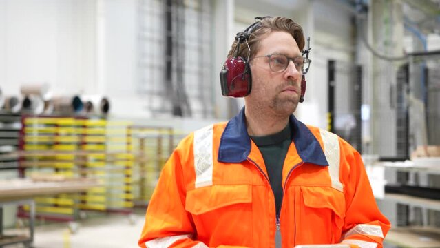 Worker in safety gear and ear protection walks through factory