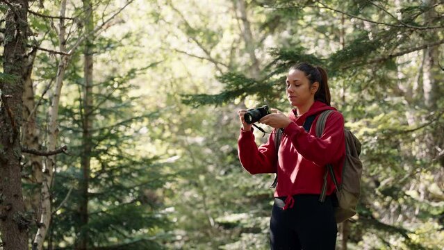 Young woman with backpack hiking in forest taking pictures
