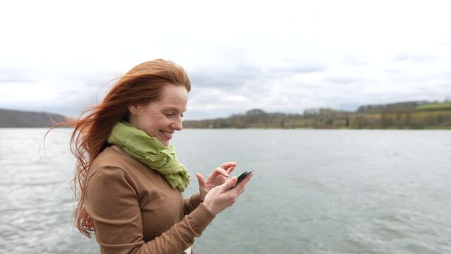 red-haired woman smiling achecking smartphone while enjoying nature
