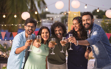 Group of youthful Friends saying happy new year by holding champagne glassless during 2024 party celebration - concept of friendship, nightlife and evening gathering