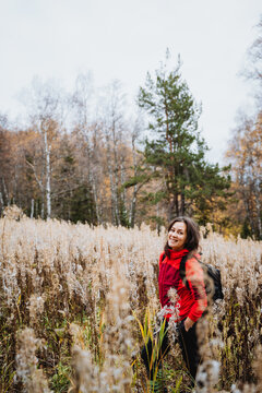 Beautiful girl in red clothes standing in dried grass in the middle of the ece, young woman smiling at the camera, trekking in the mountains with backpack. Solo travel.