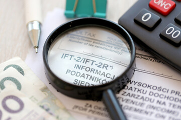 Information on revenue income derived by legal persons having no seats or place of management on territory of Poland IFT-2, IFT-2R form on accountant table with pen and polish zloty money bills