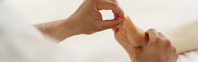 Close up of therapist masseuse massaging foot of client in spa salon during rehabilitation session