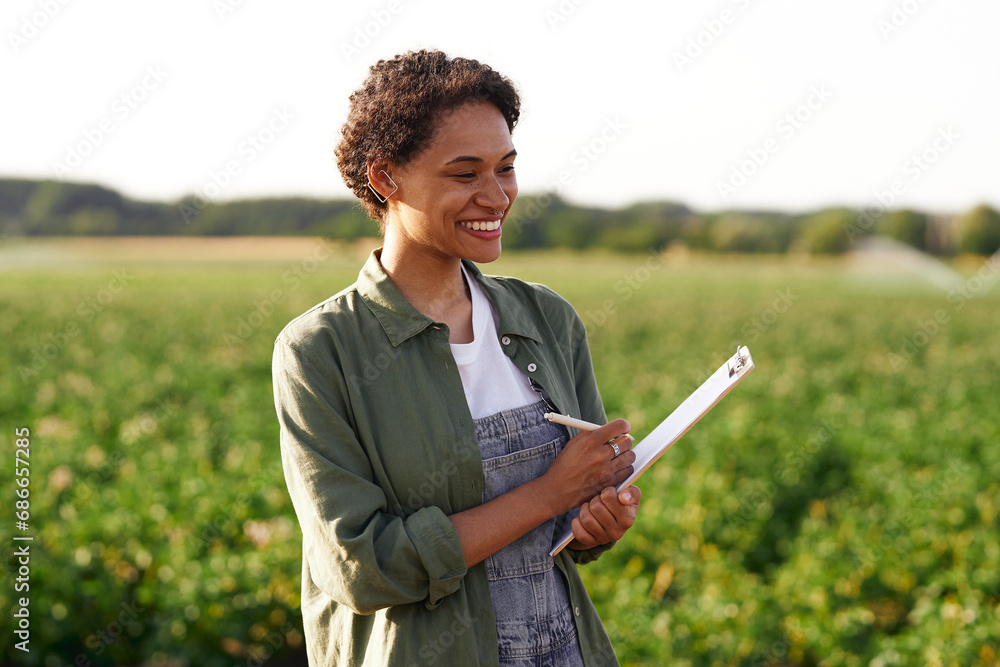 Wall mural Smiling female farmer making notes in clipboard on field during harvesting. Agricultural concept