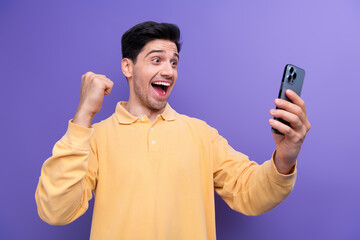 Photo of excited lucky man dressed yellow shirt winning game modern device rising fist isolated purple color background