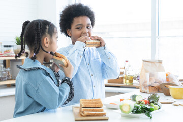 African children holding homemade sandwiches in hands and eating together in kitchen at home. Cute...