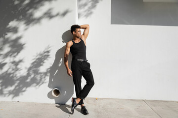 sexy cuban man in eyeglasses and black sleeveless t-shirt posing near wall in Miami, during summer