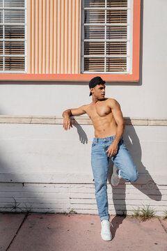 Sexy cuban man with muscular body in baseball cap and jeans standing on street in Miami
