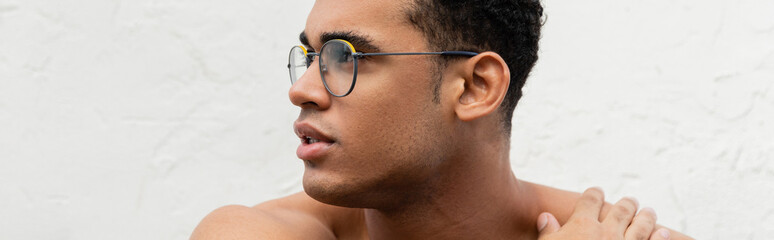 Portrait of shirtless cuban man in stylish round-shaped eyeglasses touching shoulder, banner