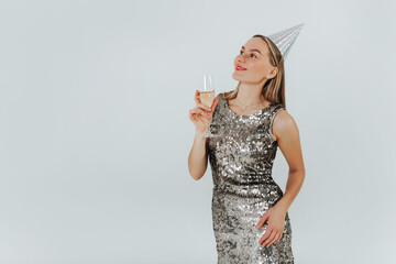 Dreaming caucasian blonde woman with wine glass wearing silver glitter dress and party hat...
