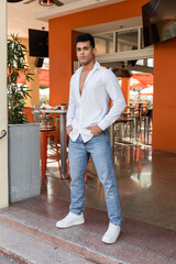 Full length of cuban man in white shirt and jeans posing in outdoor cafe on urban street in Miami