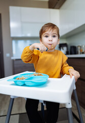 A young boy sitting in a high chair eating food. A Curious Toddler's First Solo Meal