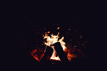 A large bonfire with flames and sparks flying upward at night on a dark background