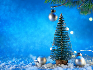 A small Christmas tree in the snow on a blue background. Christmas card