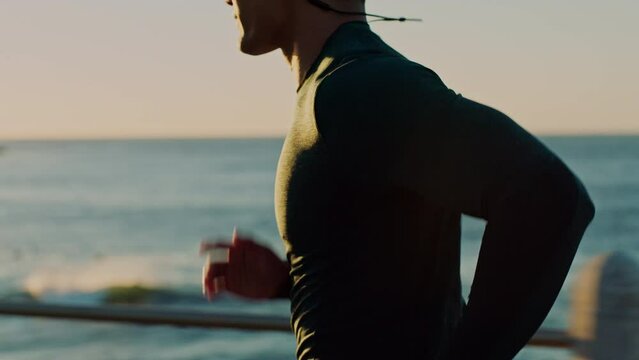 Fitness, beach or sports man running or training for a marathon with cardio exercise or workout in Sydney. Ocean, earphones or healthy athlete runner listening to music, radio or podcast at sunset