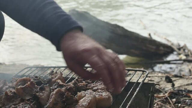 hand turns over pieces of hot meat with an appetizing crust, from pork neck, on the river bank