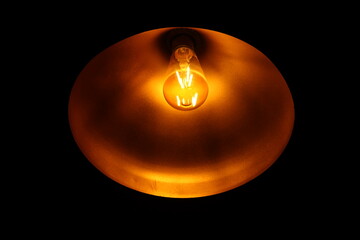 Closeup of A Black metal bowl pendant spot light illuminated by yellow filament led light bulb in...