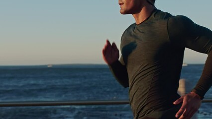 Asian man, running and earphones by beach for sunset workout, training and exercise for health, fitness and wellness. Japanese athlete, sprinting and cardio by ocean sea with music, podcast and radio - Powered by Adobe